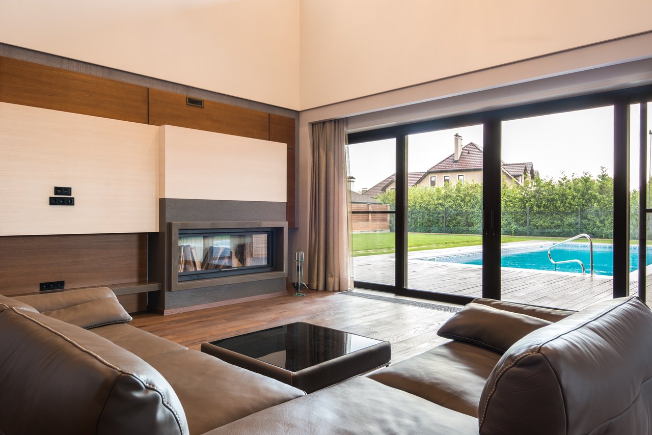services-01 Spacious modern living room with glass doors opening to a poolside area.